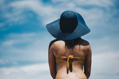 Rear view of woman in bikini wearing hat while standing against sky during sunny day