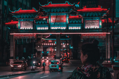 Rear view of young woman standing on illuminated street at night