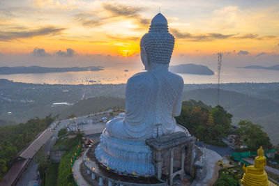 Statue against temple and building against sky during sunset