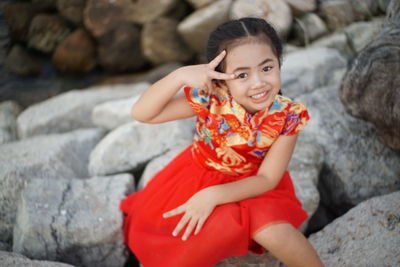 Portrait of smiling girl gesturing on forehead while sitting on rock