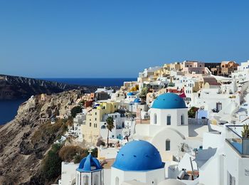 Buildings by sea against clear blue sky