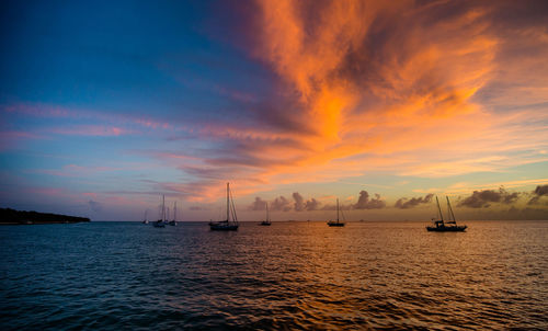 Sailboats sailing in sea against dramatic sky during sunset