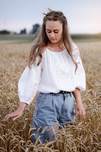 Woman walking on wheat golden field holding heap of rye. fashionable female touching wheatear