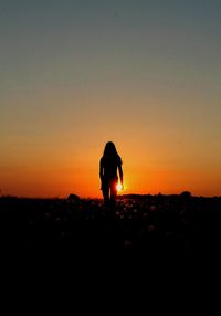 Silhouette woman standing on landscape against orange sky
