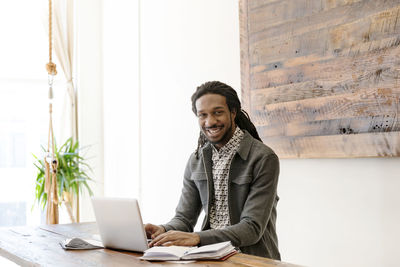 Portrait of happy young businessman working on laptop in creative office