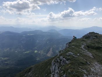 Scenic view of mountains with woman siting on grass against sky