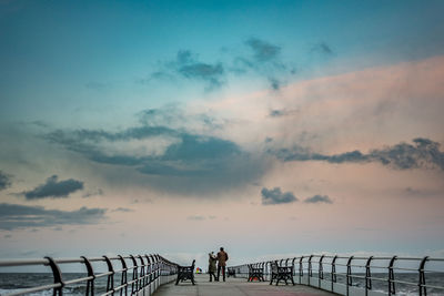 People walking on bridge against sky during sunset