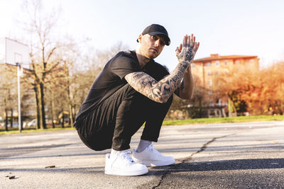 Portrait of young man crouching on land in city