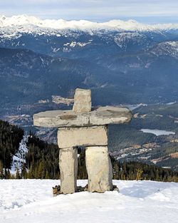 Inuksuk on snow covered field by mountains