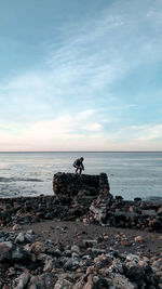 Man on rocks at beach against sky