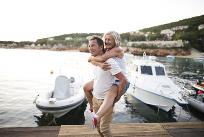 Senior man giving his wife a piggyback ride on a jetty