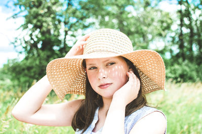 Girl in a green field wearing a floppy sun hat on a bright summer day