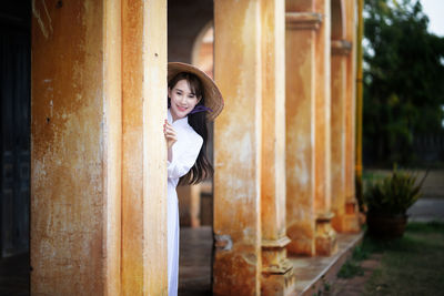 Portrait of smiling young woman wearing hat while standing in corridor