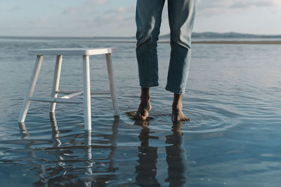 Man with white stool standing at waterfront against sky