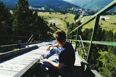 High angle view of man sitting on wooden footpath against landscape