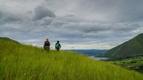 Rear view of two women on landscape against cloudy sky