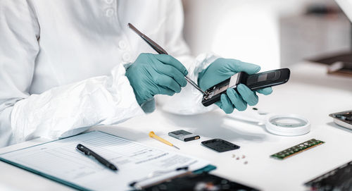 Midsection of detective repairing mobile phone on table