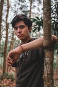 Portrait of young man standing by tree trunk in forest