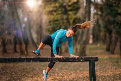 Full length of woman exercising on bench in forest