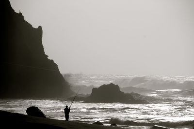 Silhouette people fishing in sea against clear sky