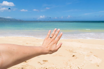Close-up of hand at beach against sky