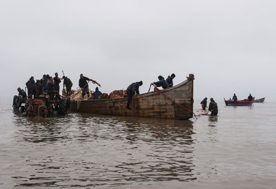 People on boats in sea against clear sky