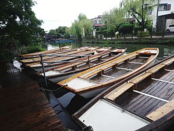 Boats moored by trees against sky