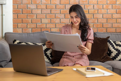 Young woman using phone while sitting on sofa