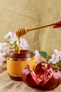 Cropped hand holding honey dipper with pomegranate on table