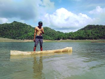 Full length of shirtless man standing in lake against sky