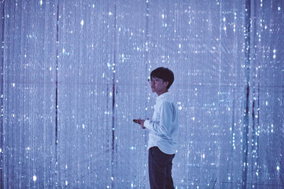 Man holding smart phone while standing against blue wall