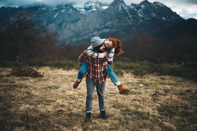 Lovely couple hugging and spending time together piggybacking and traveling in lawn with dry grass near by mountains in cloudy day