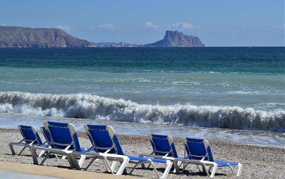 Deck chairs on beach against sky