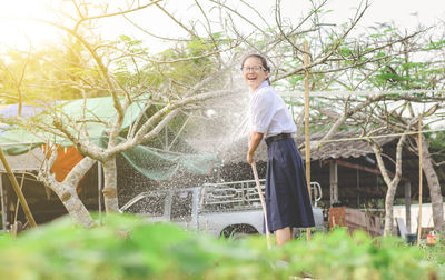 Water spraying on cheerful woman standing at park