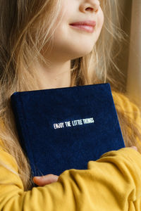Young girl holding a book with text - enjoy the little things.