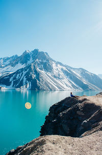 Full length of woman sitting by lake against mountain and sky