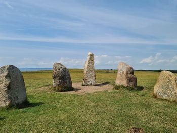 Swedish stonehenge site on green field ad shore against sky