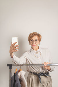 Portrait of young woman using mobile phone while standing against white background