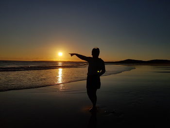 Silhouette man standing at beach against sky during sunset