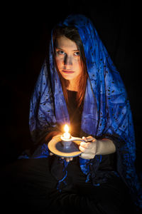 Young woman holding candle against black background