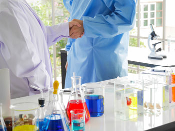 Midsection of scientists holding hands at laboratory