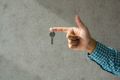 Close-up of man holding key against wall