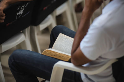 Midsection of man reading book while sitting on chair
