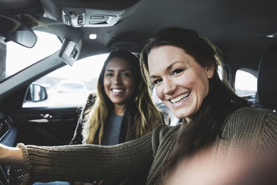 Portrait of smiling friends sitting in car at showroom