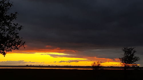 Silhouette trees against dramatic sky during sunset