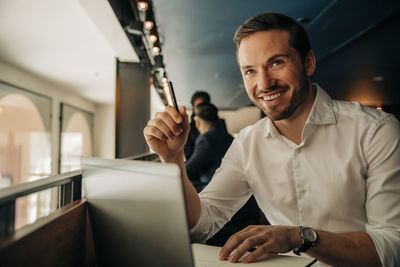 Happy male entrepreneur looking away while sitting with laptop in hotel