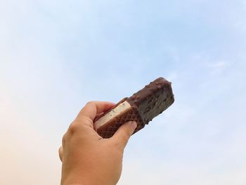 Close-up of hand holding bread against sky