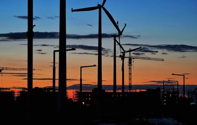 Silhouette cranes at construction site against sky during sunset