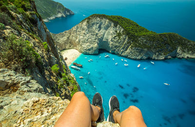 Low section of person sitting at cliff by sea