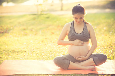 Pregnant woman touching belly while sitting on field